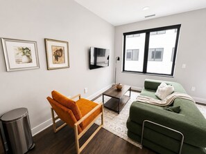 A modern living room with a sofa, a chair, a TV, and artwork on the walls. - Sleepover | Urban Studio + Gym/Sauna - Omaha (Omaha)