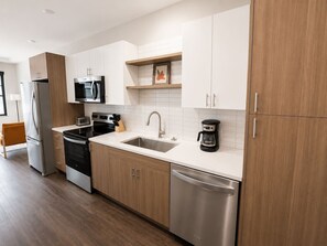 A modern kitchen with stainless steel appliances, wooden cabinets, and a white countertop. - Sleepover | Airy Studio + Gym/Sauna - Omaha (Omaha)