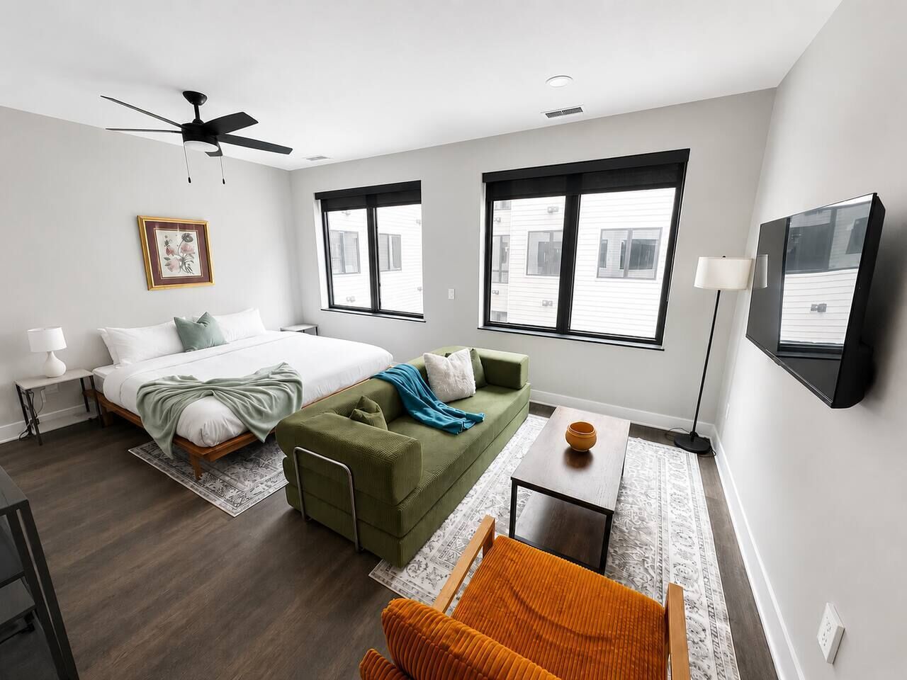 Ein modernes Schlafzimmer mit einem Bett, einem grünen Sofa, einem kleinen Tisch und einem an der Wand befestigten Fernseher.