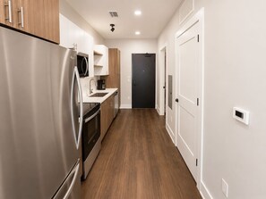 Une cuisine moderne dotée d’appareils électroménagers en acier inoxydable, de meubles en bois et d’une porte sombre au bout du couloir.