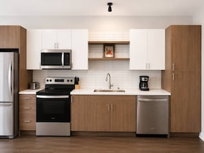 Uma cozinha moderna com eletrodomésticos de aço inoxidável, armários de madeira e bancada branca.