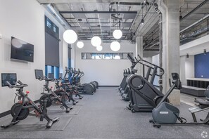 Une salle de sport équipée de plusieurs vélos d’exercice et tapis de course, disposés en rangées.