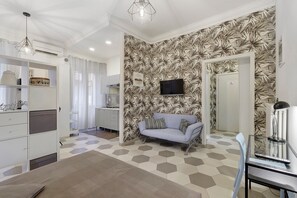 A modern living room with a sofa, a television mounted on a leaf-patterned wall, and a dining area with a table and chairs. - Domus San Pietro B Apartment in Rome – Comfort for Up to 3 Guests (Rome)