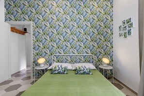 Ein Schlafzimmer mit ornamentalem Wandpapier, einem Bett mit zwei Kissen, Nachttischlampen und einem kleinen Tisch.
