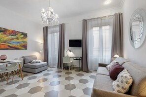 A modern living room with a sofa, a dining table, a TV, and a painting on the wall. - Domus San Pietro Scala C Apartment (Rome)