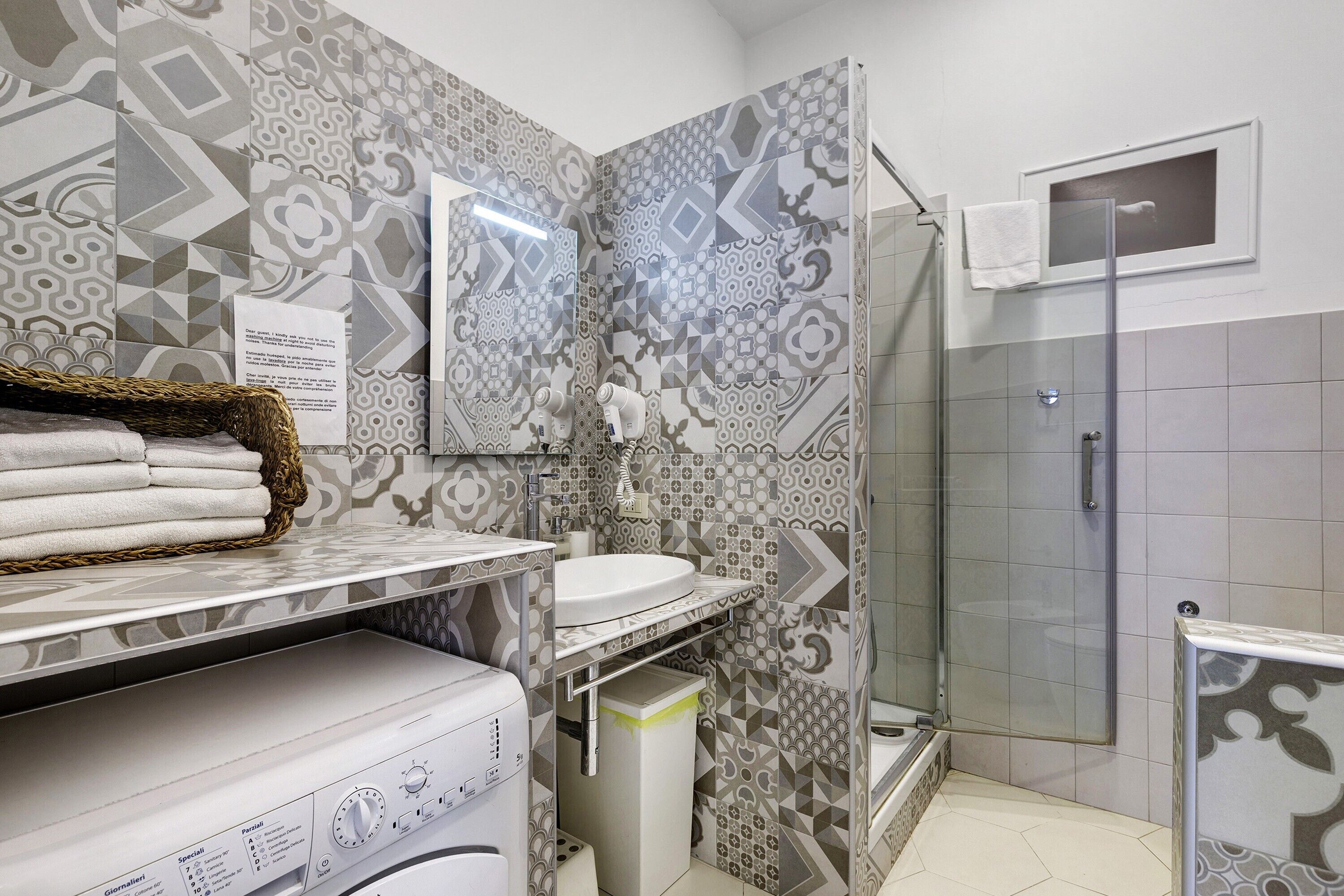 A bathroom with patterned tiles, a sink, a mirror, a towel rack, and a shower area.