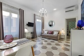 A modern hotel room with a sofa, a dining table, a TV, and a chandelier. - Domus San Pietro Scala C Apartment (Rome)