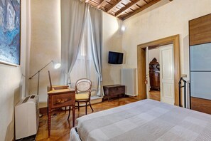 Un dormitori amb llit, escriptori, cadira, radiador i televisió.