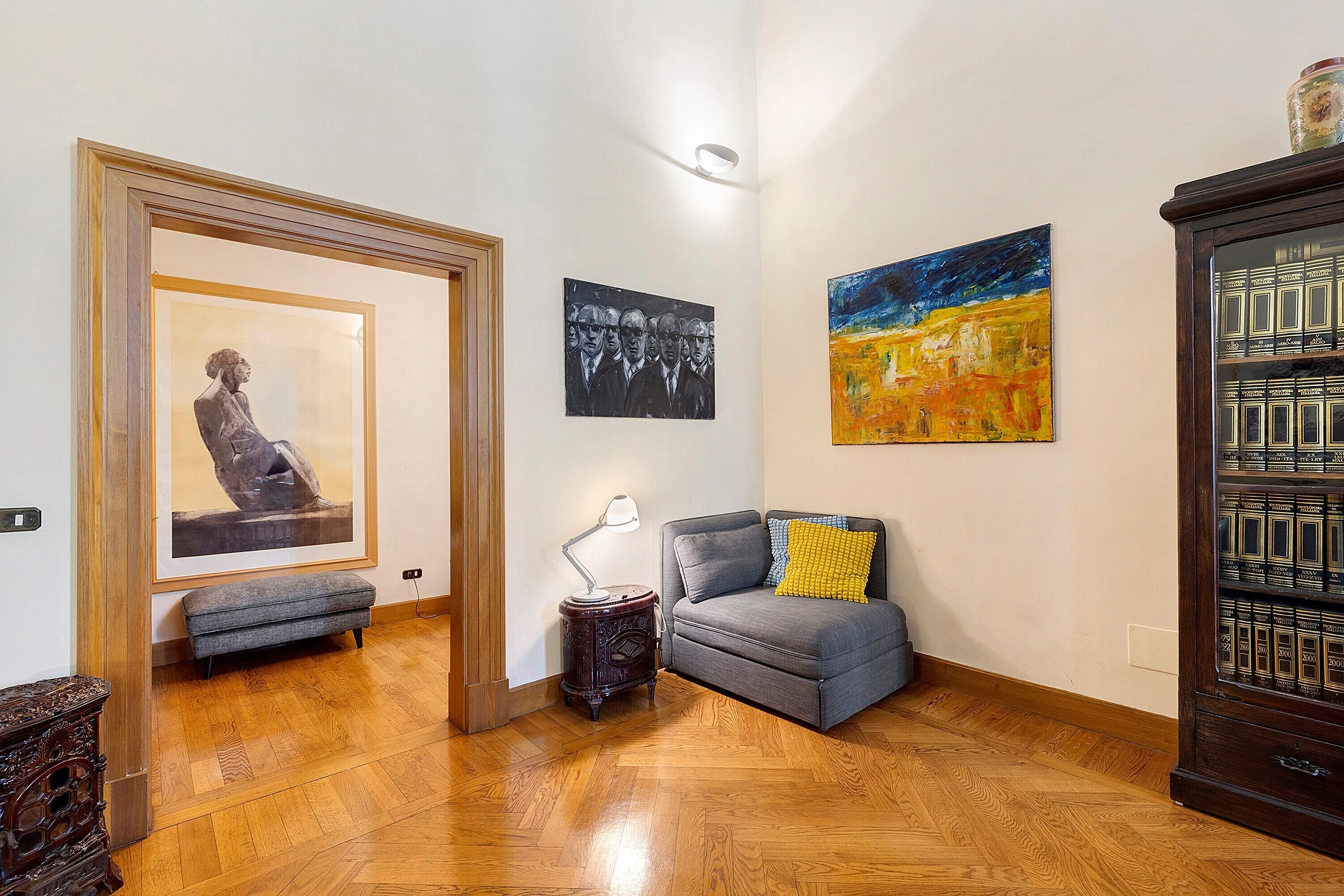 A hallway with a wooden floor, a bench, a table with a lamp, and a sofa with cushions.