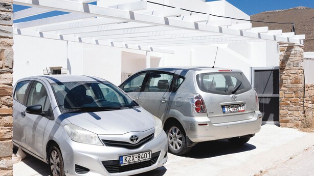 Dois carros estacionados em frente a um edifício branco com uma parede de pedra.
