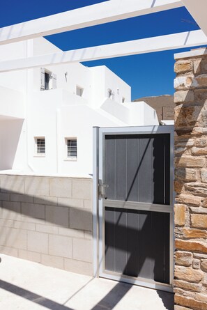 A white building with a metal door and stone wall. - Rhea Sea Breeze Studio (Paros)