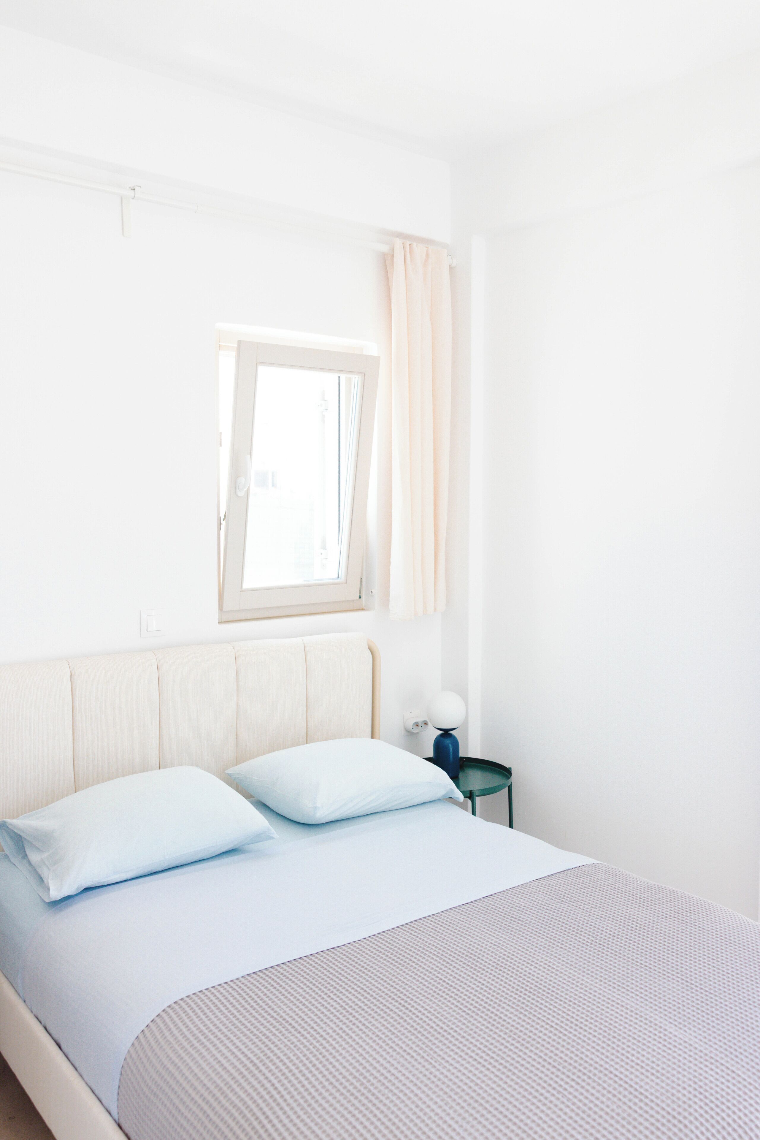 A bedroom with a bed, pillows, a nightstand, a lamp, and a window with curtains.