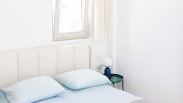 A bedroom with a bed, pillows, a nightstand, a lamp, and a window with curtains.