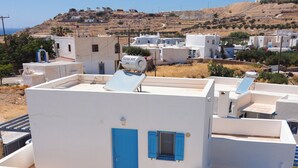 Um edifício branco com porta e janelas azuis, uma mesa branca com duas cadeiras e um aquecedor solar no telhado.