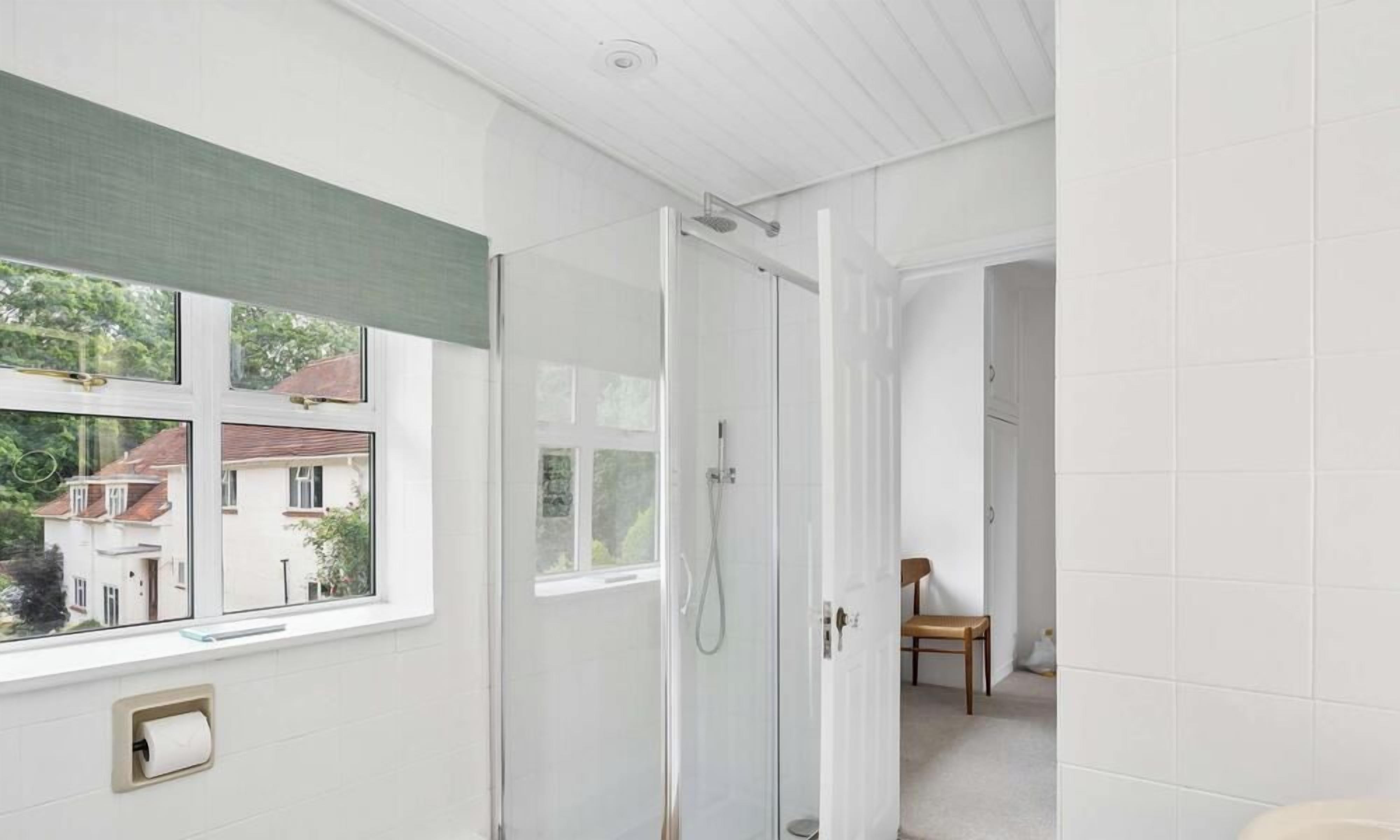 A bathroom with a shower, a toilet, and a window with a view of houses.