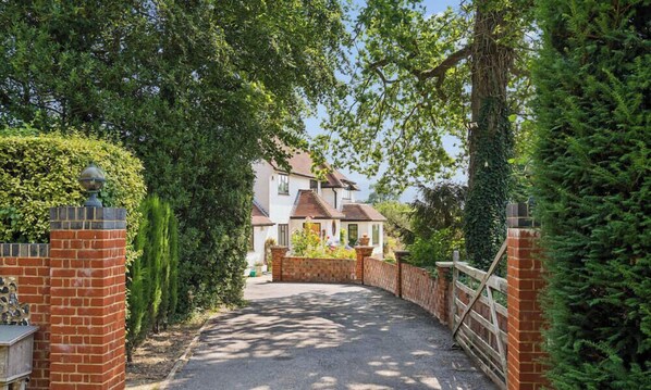 A gated driveway leading to a house with a brick wall on one side and a wooden fence on the other.