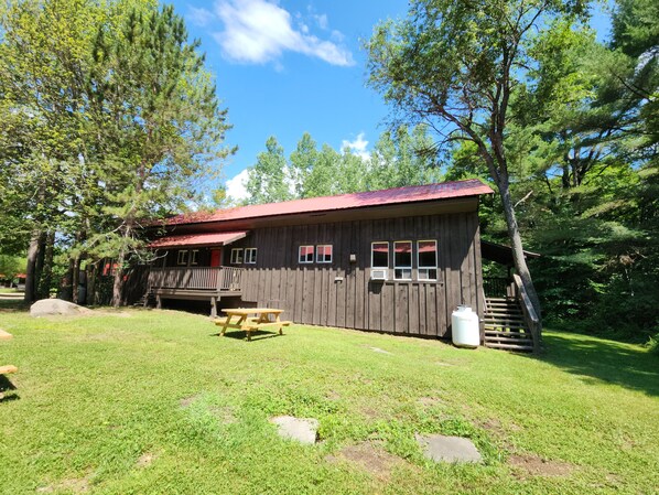 A rustic wooden cabin with a porch, a picnic table, and a staircase leading to a covered area.