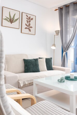 A modern living room with a white sofa, green and white cushions, a white coffee table, and a lamp. There are two framed botanical prints on the wall. - Patacona Pure. WiFi+PK+A/C+Pool (Alboraya / Alboraia)