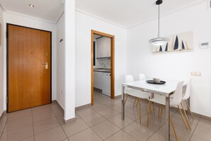 A modern kitchen with white cabinets and a dishwasher, a dining area with a white table and chairs, and a wooden door. - Patacona Pure. WiFi+PK+A/C+Pool (Alboraya / Alboraia)