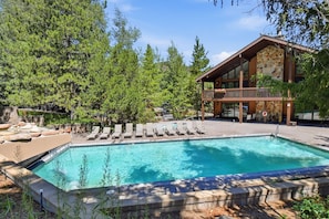 Une piscine entourée d’arbres, avec des chaises longues, et un bâtiment doté d’un balcon.