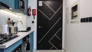 A modern kitchen with a built-in oven, microwave, and stove, a washing machine, and a black door with geometric patterns. - Modern Studio with Private Pool and Balcony (Dubai)