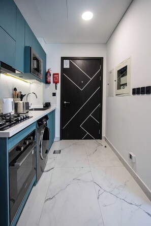 A modern kitchen with a built-in oven, microwave, and stove, a washing machine, and a black door with geometric patterns. - Modern Studio with Private Pool and Balcony (Dubai)