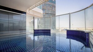 A modern indoor swimming pool with a curved design, large windows, and a view of a tall building. - Modern Studio with Private Pool and Balcony (Dubai)