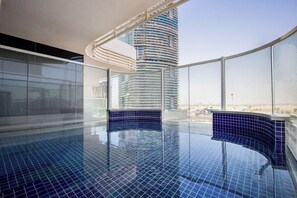 A modern indoor swimming pool with a curved design, large windows, and a view of a tall building. - Modern Studio with Private Pool and Balcony (Dubai)