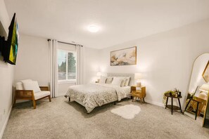 Ein Schlafzimmer mit einem Bett, einem Sessel, einem Nachttisch, einem Spiegel und einem Fenster mit Vorhängen.
