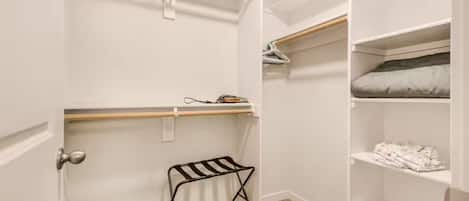 A walk-in closet with open shelving, a hanging rod, and a small stool.