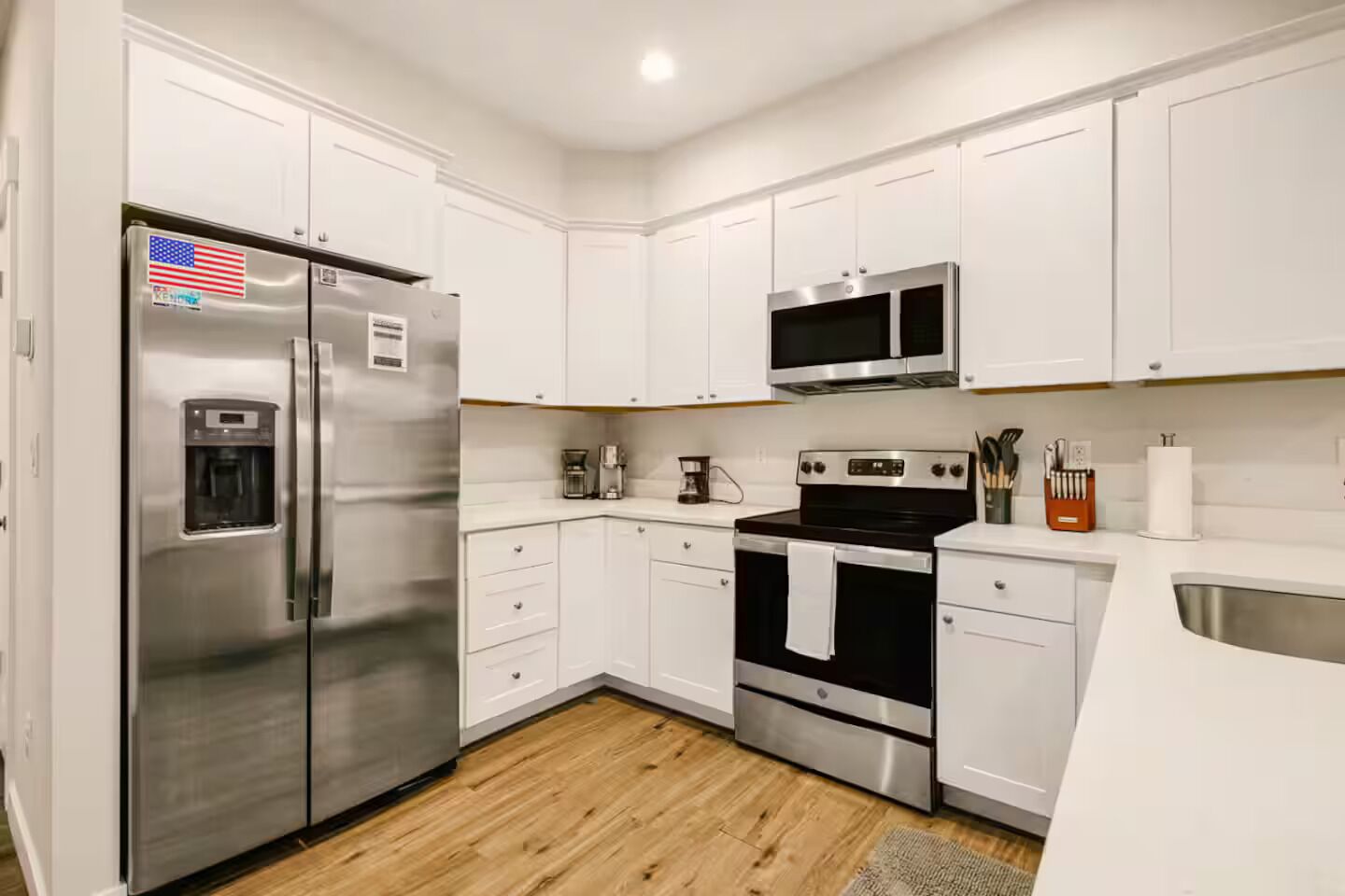 A modern kitchen with white cabinetry, stainless steel appliances, and a wooden floor.