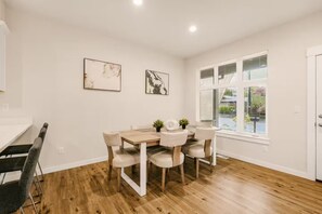 Ein Essbereich mit Holztisch und -stühlen, einem Fenster mit Jalousien und zwei gerahmten Kunstwerken an der Wand.