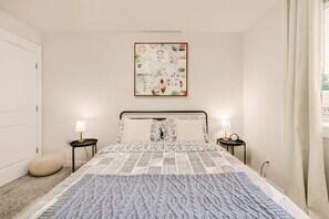 Ein Schlafzimmer mit einem Bett, zwei Nachttischen, einem Wandbild und einem Fenster mit Vorhängen.