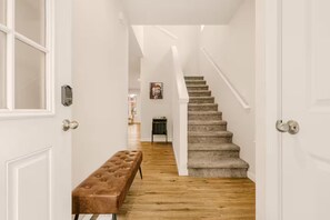 Ein Flur mit einer hölzernen Bank, einem Teppich und einer Treppe sowie einer Tür mit Zahlenschloss.
