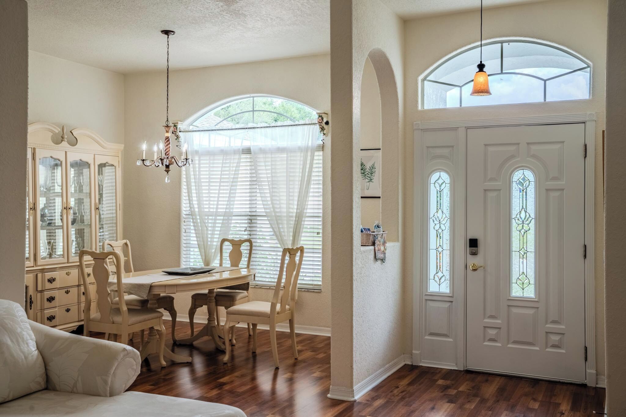 A dining area with a table and chairs, a chandelier, and a window with blinds.