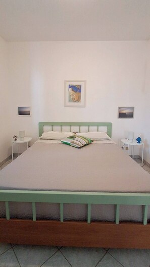 Ein Schlafzimmer mit einem Bett, Kissen, einem Nachttisch, einer Lampe und einem Bild an der Wand.