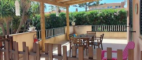 An outdoor patio with a wooden pergola, tiled flooring, and a seating area with chairs and a table.