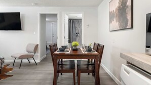 A modern dining area with a wooden table, four chairs, and a flat-screen TV mounted on the wall. - The Weekender | Cozy Bridgeland Retreat | Sleeps 2 (Calgary)