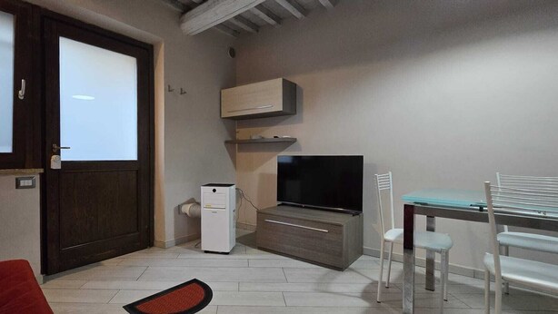 Een compacte woonruimte met een televisie, een kleine koelkast, een eettafel met stoelen en een deur met geëtste glaspanelen.