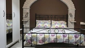 Uma cama com estrutura de metal e colcha estampada, um arco branco na porta e uma parede de pedra.