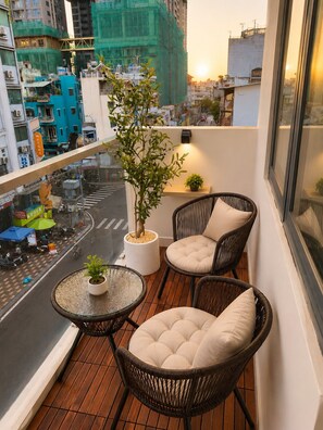 A balcony with wicker chairs and a small table, overlooking a city street with buildings and a clear sky. - Aurora Stay Inn Saigon (Ho Chi Minh City)