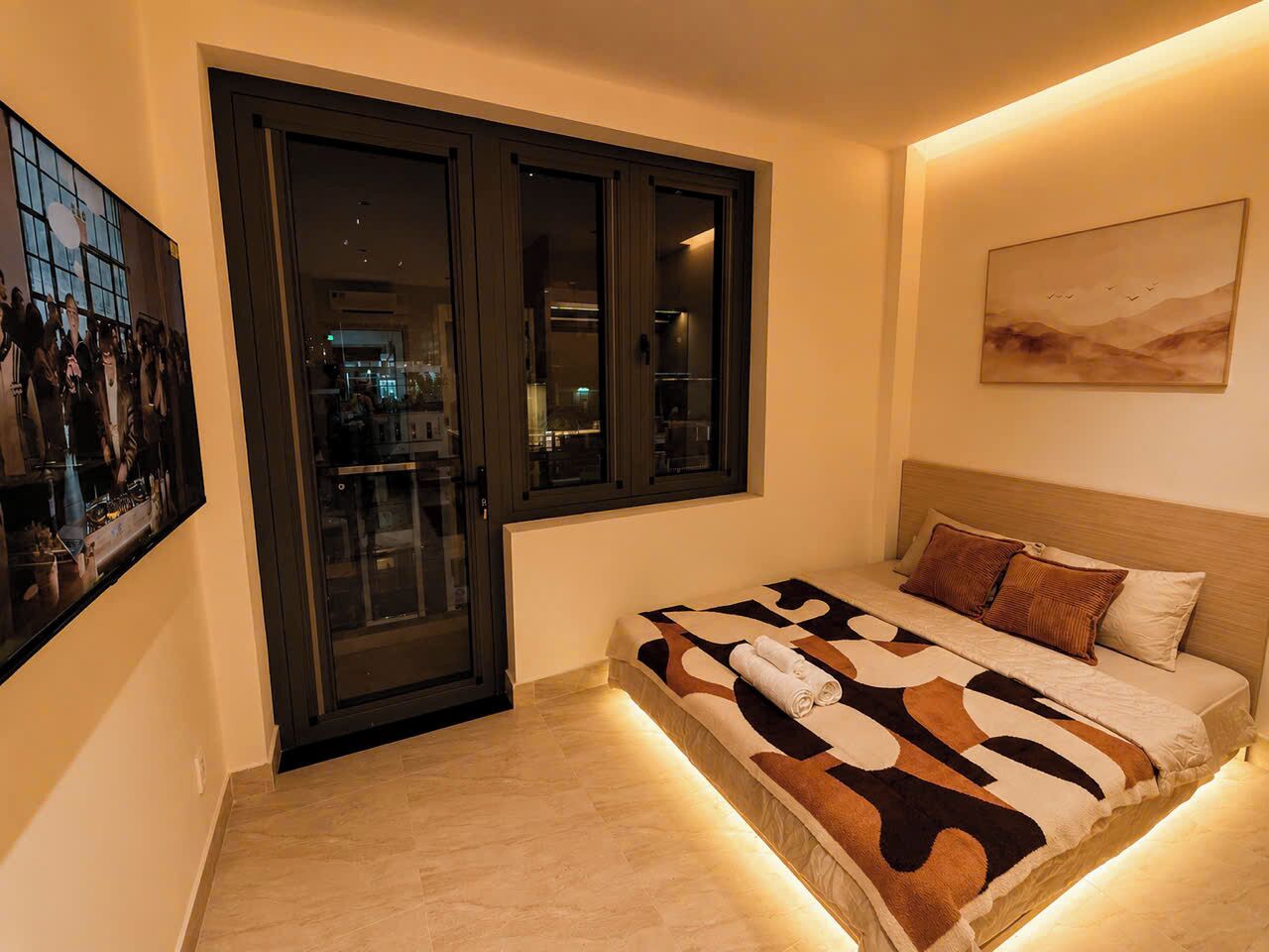 Un dormitorio con una cama, un ventanal grande y un cuadro en la pared.