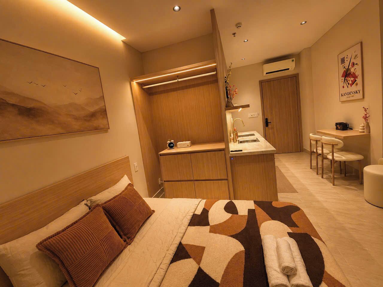 A hotel room with a bed, a desk, a chair, and a small kitchenette.