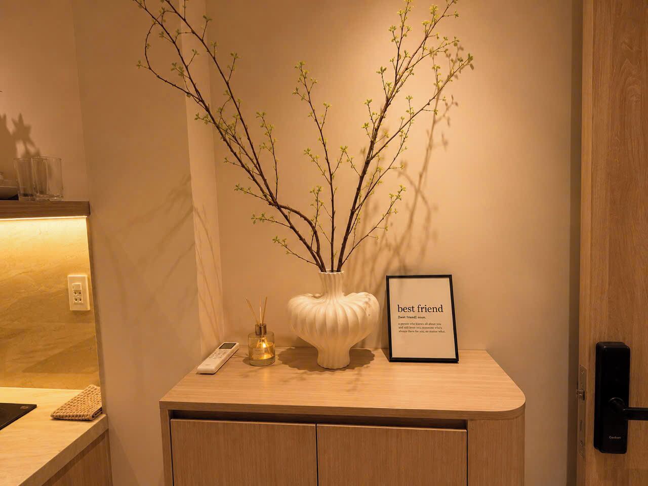 A reception desk with a framed sign that reads 'best friend,' a vase with branches, a bottle of perfume, and a remote control.