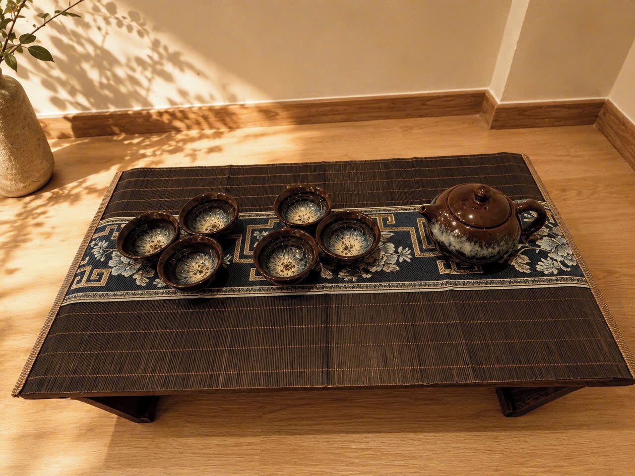 Een traditionele theeset op een geweven mat met een geometrisch patroon, geplaatst op een houten vloer.