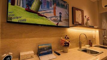A kitchen with a TV mounted above the counter, a clock, a calendar, and a vase with flowers.