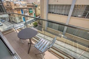 Ein Balkon mit einem Metalltisch und Stuhl, der auf eine Straße mit Gebäuden blickt.