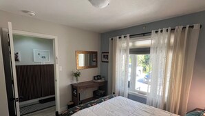 Un dormitorio con cama, mesita de noche, espejo y ventana con cortinas.