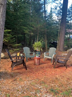 An outdoor seating area with four Adirondack chairs, a small table with a plant, and a tree stump.