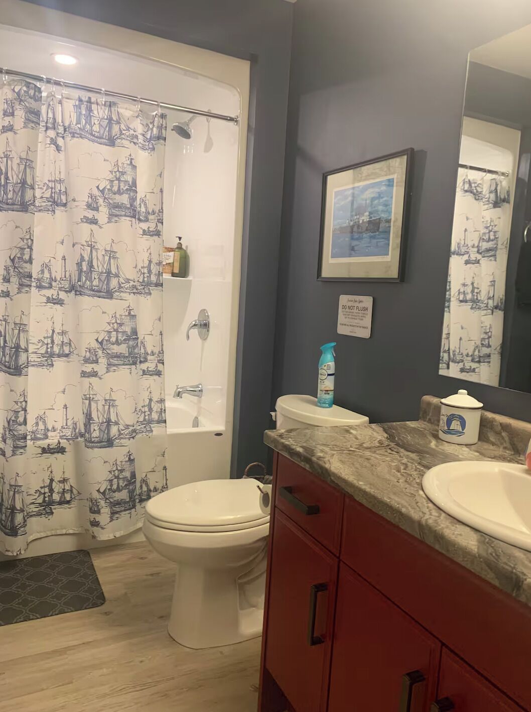 Une salle de bain avec un rideau de douche orné de motifs marins, des toilettes, un lavabo avec un plan de travail en marbre et un tableau encadré accroché au mur.